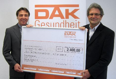 Eine Geldspritze für den Infostand der DHS an der RehaCare 2013 Zwei Männer halten gemeinsam den Riesen-Spendenscheck